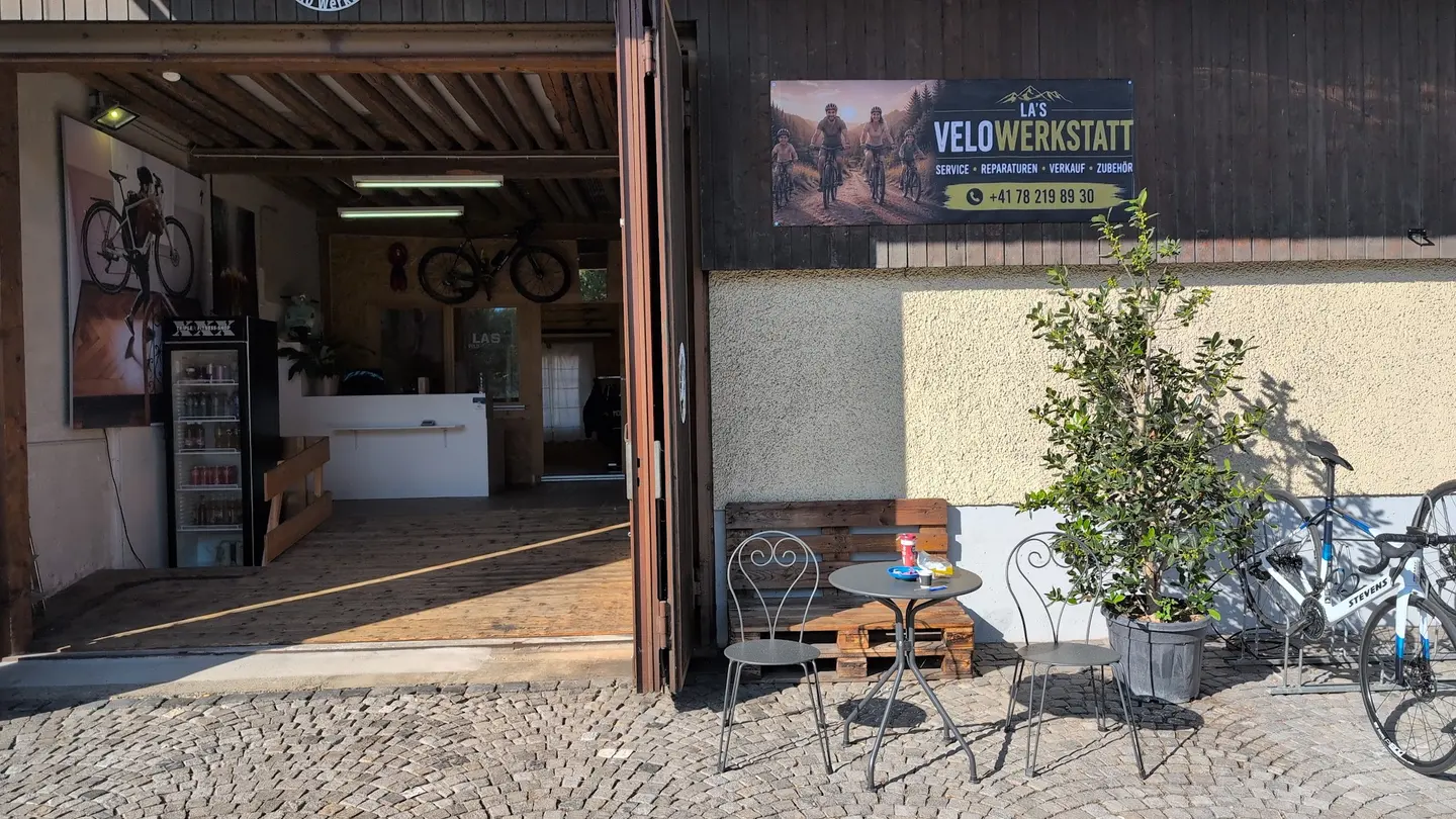 Das offene Tor der Werkstatt, davor ein Tischchen mit zwei Stühlen